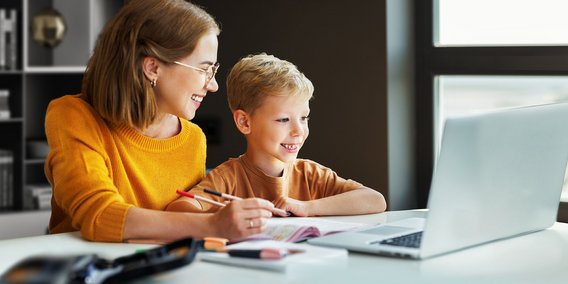 Mutter und Sohn lachend vor Laptop und Arbeitsheft