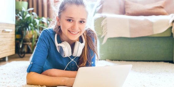 Schülerin liegt mit Laptop und Kopfhörer auf dem Boden