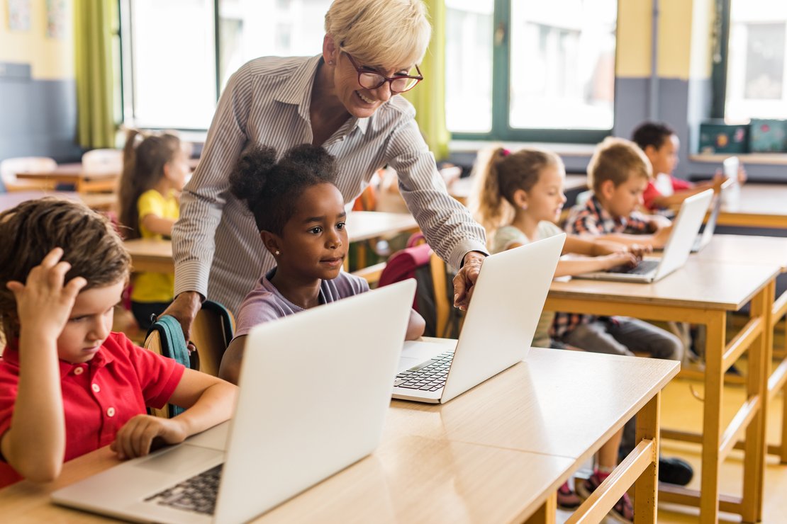 Lehrerin mit Schüler/innen an Laptops