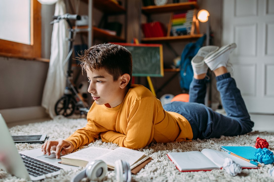 Schüler liegt mit Laptop und Schulsachen auf dem Boden