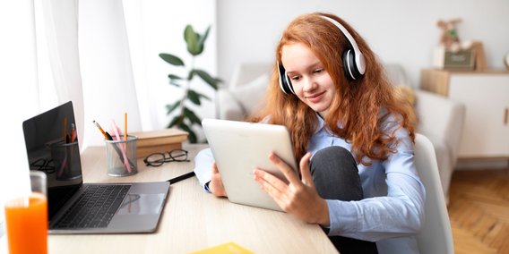 Mädchen mit Tablet und Kopfhörern am Schreibtisch